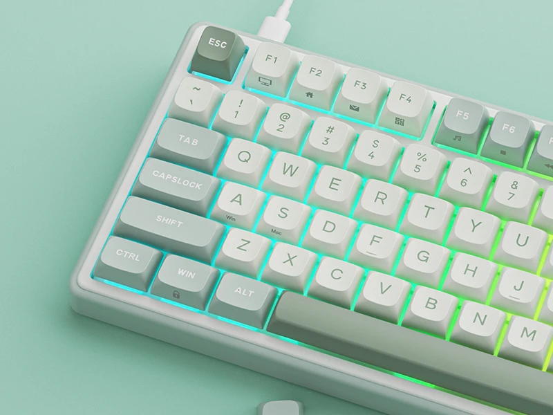 Na obrazie widoczna jest klawiatura z podświetleniem w kolorze miętowym. Klawisze mają oznaczenia takie jak ESC, TAB, CAPSLOCK, SHIFT, CTRL, WIN, ALT oraz litery i cyfry.