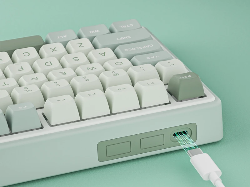 Na obrazie widoczna jest klawiatura z klawiszami w odcieniach zieleni i bieli. Widać także podłączony kabel USB oraz dwa przyciski na boku obudowy.