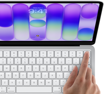 Laptop z widocznym ekranem wyświetlającym kolorowe gradienty i zegar z godziną 9:41 oraz datą Wed Apr 9. Na klawiaturze znajduje się dłoń naciskająca klawisz w prawym górnym rogu.
