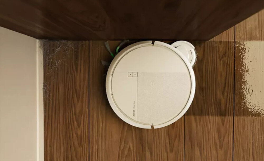 Na drewnianej podłodze znajduje się biały robot sprzątający z widocznym logo \'iRobot Roomba\'.