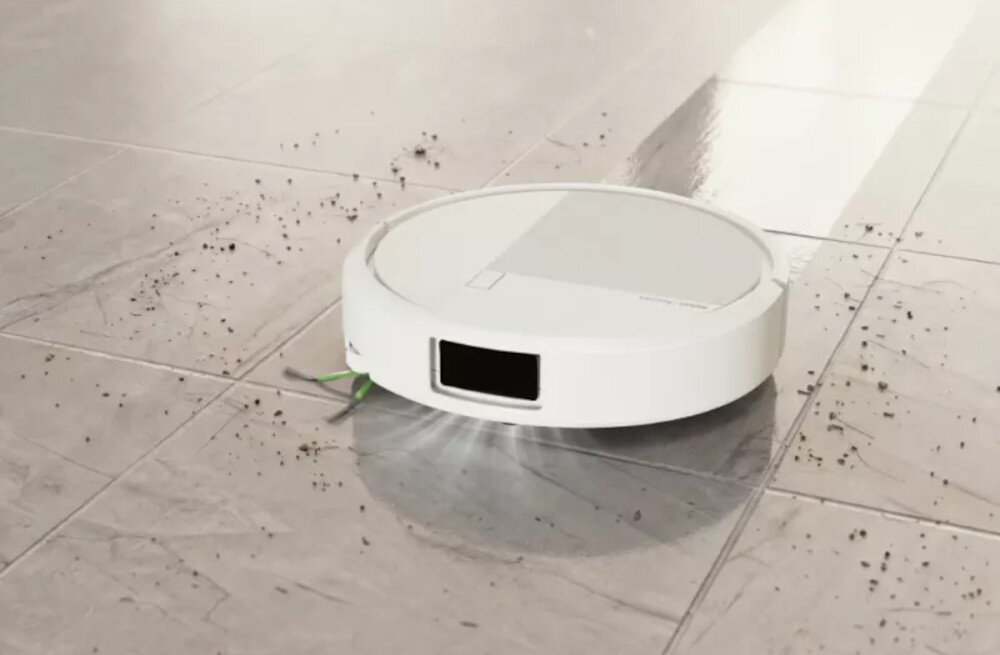 Biały robot sprzątający porusza się po podłodze, zbierając widoczne zabrudzenia. Podłoga jest częściowo czysta, a częściowo pokryta kurzem i brudem.