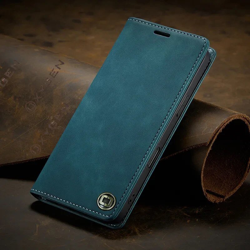 Na obrazie widoczne jest etui na telefon w kolorze niebieskim, z metalowym logo w dolnym rogu. W tle znajduje się materiał z wytłoczonym napisem \'OXYGEN\'.