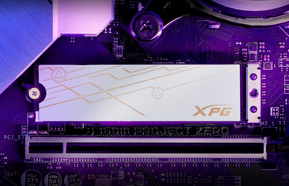 Na obrazie widoczny jest dysk SSD z logo \'XPG\' zamontowany na płycie głównej. Płyta główna ma fioletowe podświetlenie i widoczny napis \'PROJECT ZERO\'.