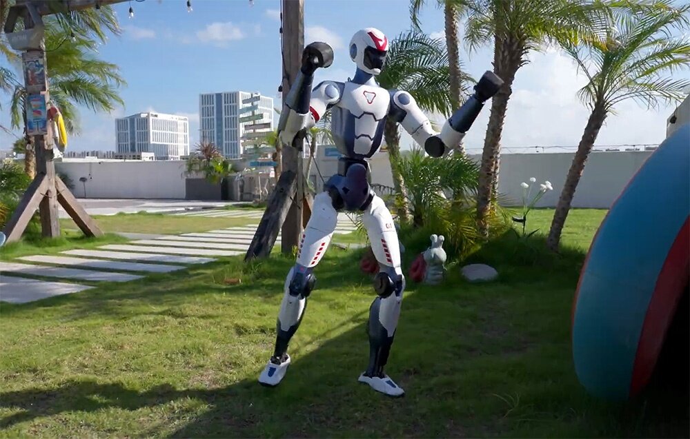 Robot humanoidalny uchwycony w półprzysiadzie wewnątrz długiego, jasnego korytarza z szarymi filarami