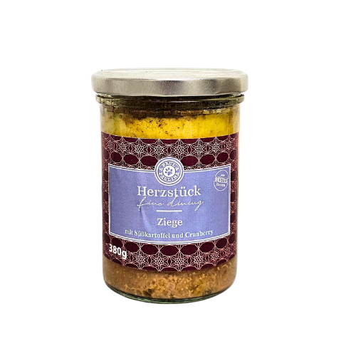 Słoik z metalową pokrywką zawiera produkt oznaczony etykietą \'Herzstück feine Ernährung Ziege mit Süßkartoffel und Cranberry 380g\'.
