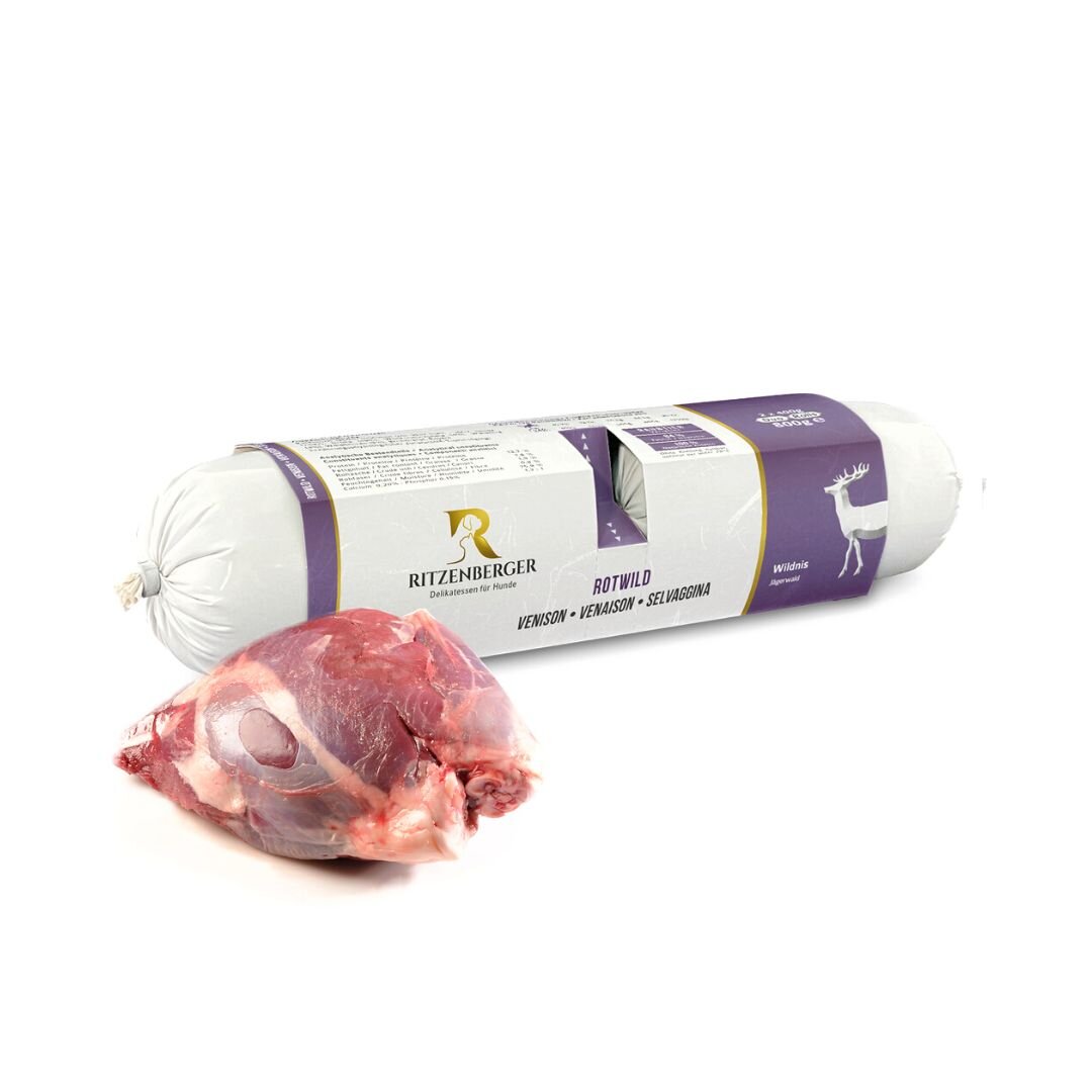 Na obrazie widoczna jest biała rolka z etykietą w kolorze fioletowym z logo Ritzenberger oraz napisem \'ROT WILD VENISON\'. Obok znajduje się kawałek surowego mięsa.