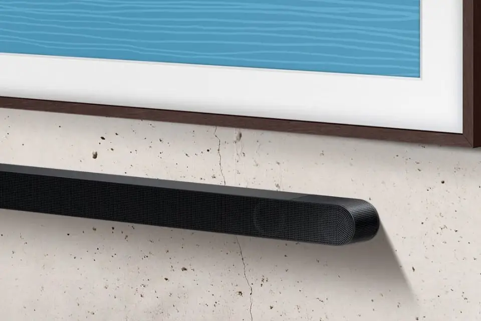 soundbar 960x640 Na obrazie widoczny jest fragment telewizora z drewnianą ramą oraz czarny soundbar zamontowany na ścianie. Ściana ma widoczne drobne pęknięcia i nierówności.