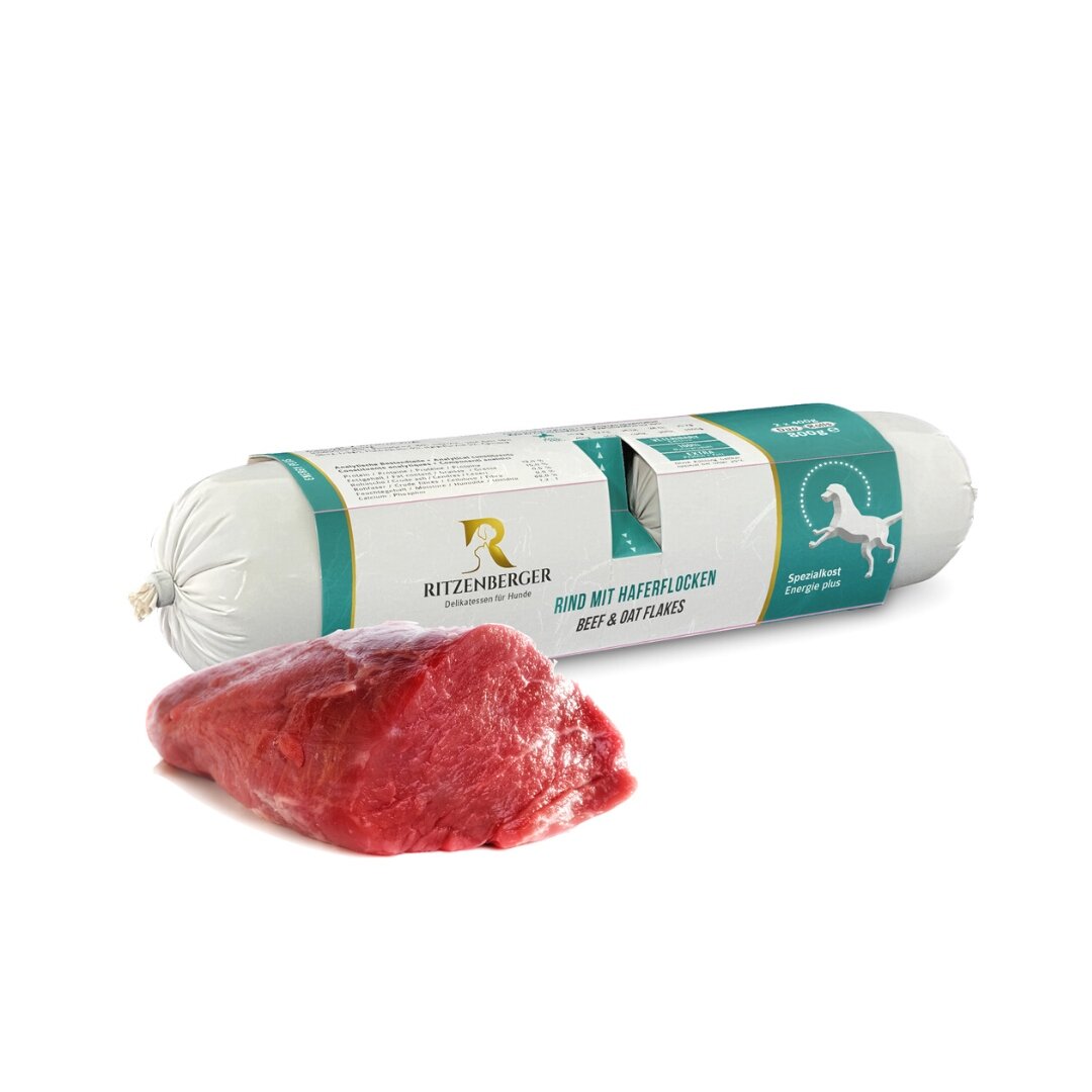 Na obrazie widoczna jest rolka karmy dla psów z etykietą \'Ritzenberger\' oraz kawałek surowego mięsa. Na etykiecie znajduje się napis \'RIND MIT HAFERFLOCKEN BEEF & OAT FLAKES\'.