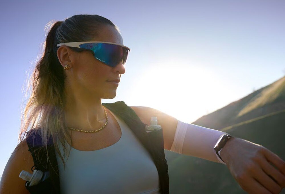 Okulary META Oakley Vanguad Kobieta w okularach sportowych patrzy w bok na tle nieba i wzgórza w świetle słońca, soczewki, filtr, technologia Prizm