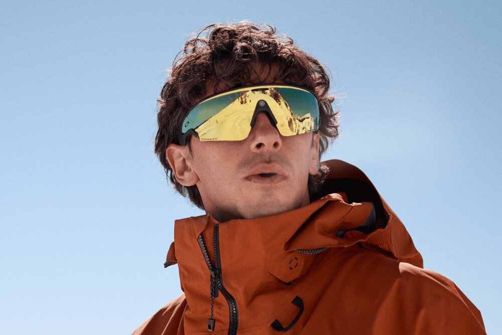 Okulary META Oakley Vanguad Mężczyzna z brodą w ciemnej koszulce i okularach przeciwsłonecznych trzyma kij golfowy na tle zielonej trawy, opis