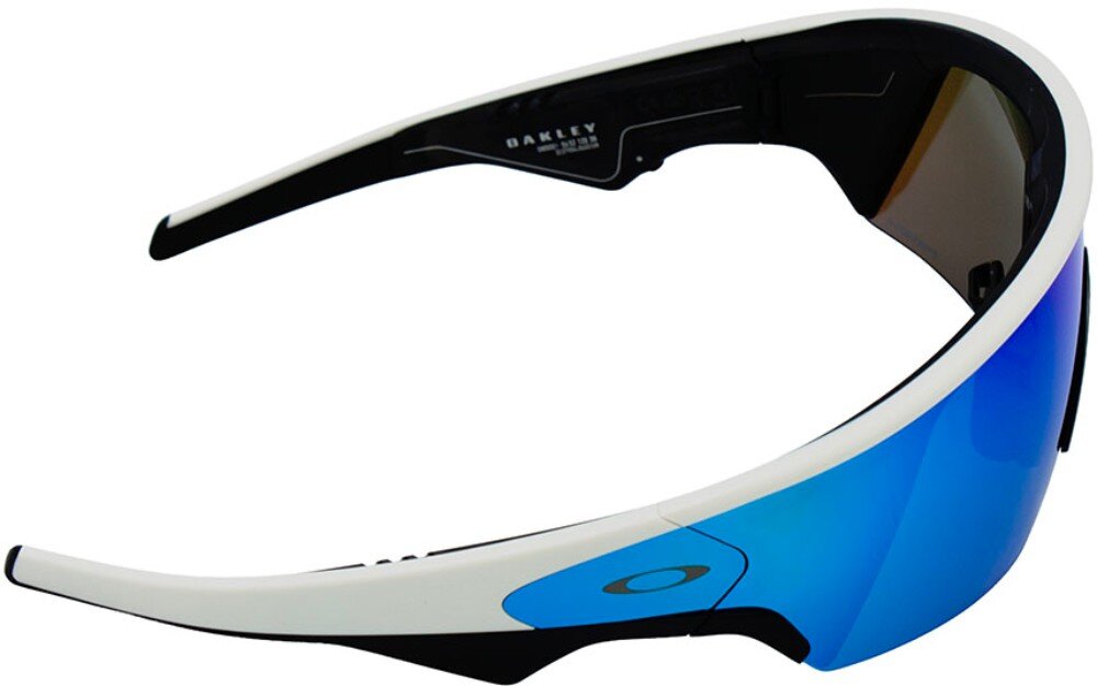 Okulary przeciwsłoneczne z białą oprawką i niebieskimi soczewkami, z widocznym logo Oakley na zauszniku. Wewnątrz oprawki znajduje się napis: \'OAKLEY MADE IN USA\'.
