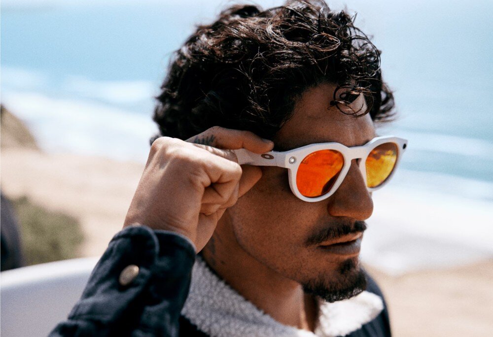 Okulary META Oakley HSTN Mężczyzna z profilu w okularach przeciwsłonecznych, oświetlony ciepłym, pomarańczowym światłem konturowym na ciemnym tle, opis