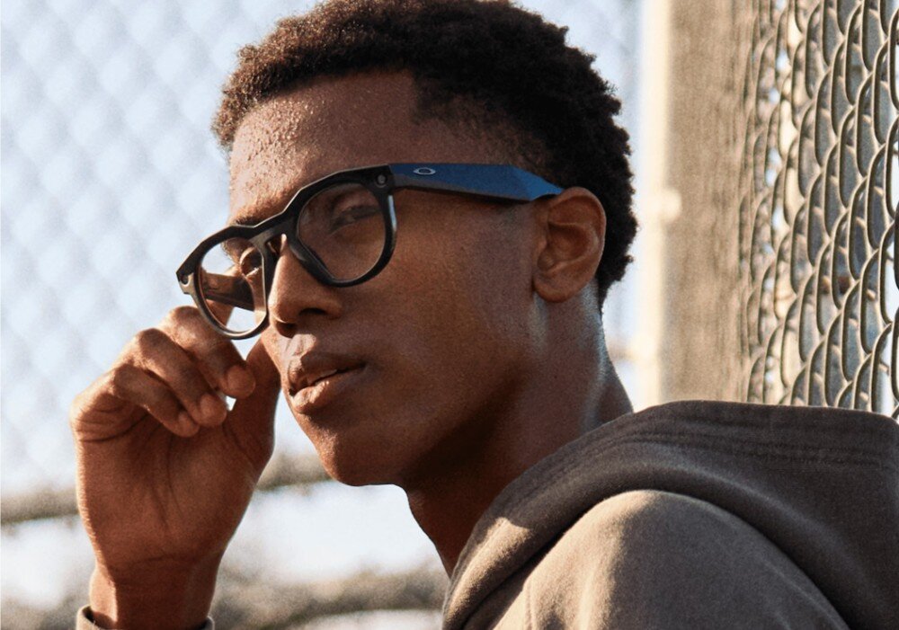 Okulary META Oakley HSTN Mężczyzna z profilu w okularach przeciwsłonecznych, oświetlony ciepłym, pomarańczowym światłem konturowym na ciemnym tle, opis
