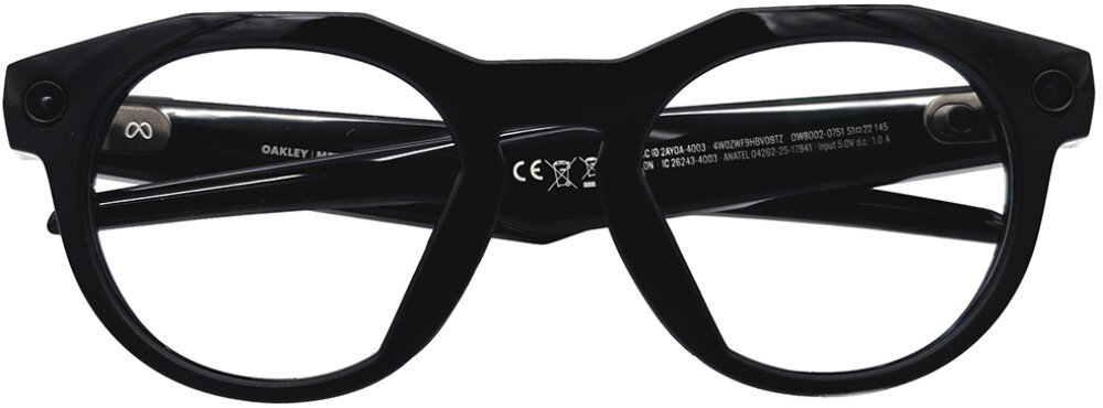 Czarne okulary z grubymi oprawkami, na zausznikach widoczne są napisy i symbole, w tym logo Oakley.