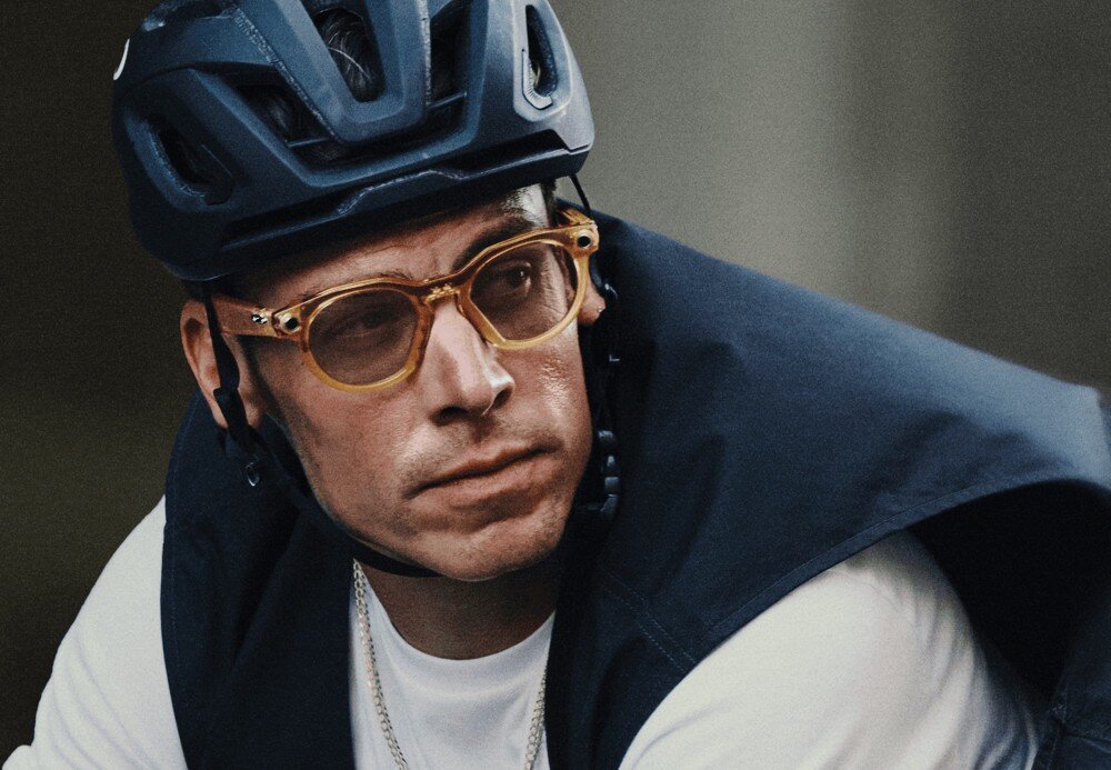 Okulary META Oakley HSTN Mężczyzna z profilu w okularach przeciwsłonecznych, oświetlony ciepłym, pomarańczowym światłem konturowym na ciemnym tle, opis