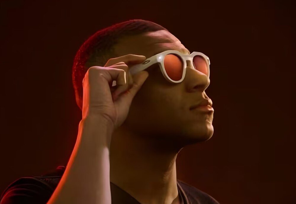 Okulary META Oakley HSTN Mężczyzna patrzący w bok i podnoszący dłonią okulary przeciwsłoneczne, sfotografowany w ciepłym oświetleniu studyjnym, komendy głosowe, funkcje, obsługa