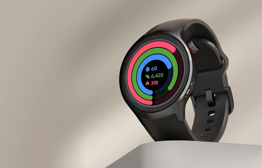 Czarny smartwatch z okrągłym wyświetlaczem pokazuje kolorowe okręgi i dane: \'60\', \'6,425\', \'318\'. Urządzenie leży na jasnej powierzchni.