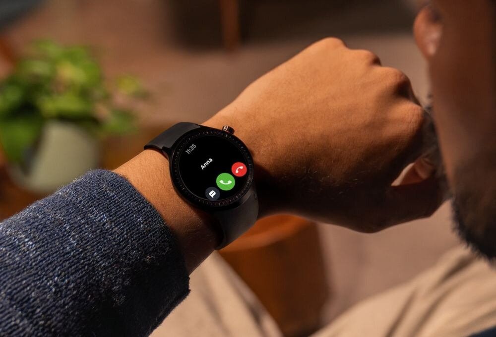 Osoba nosi czarny smartwatch z wyświetlaczem pokazującym połączenie przychodzące od \'Anna\'. Na ekranie widoczne są ikony odbierania i odrzucania połączenia.
