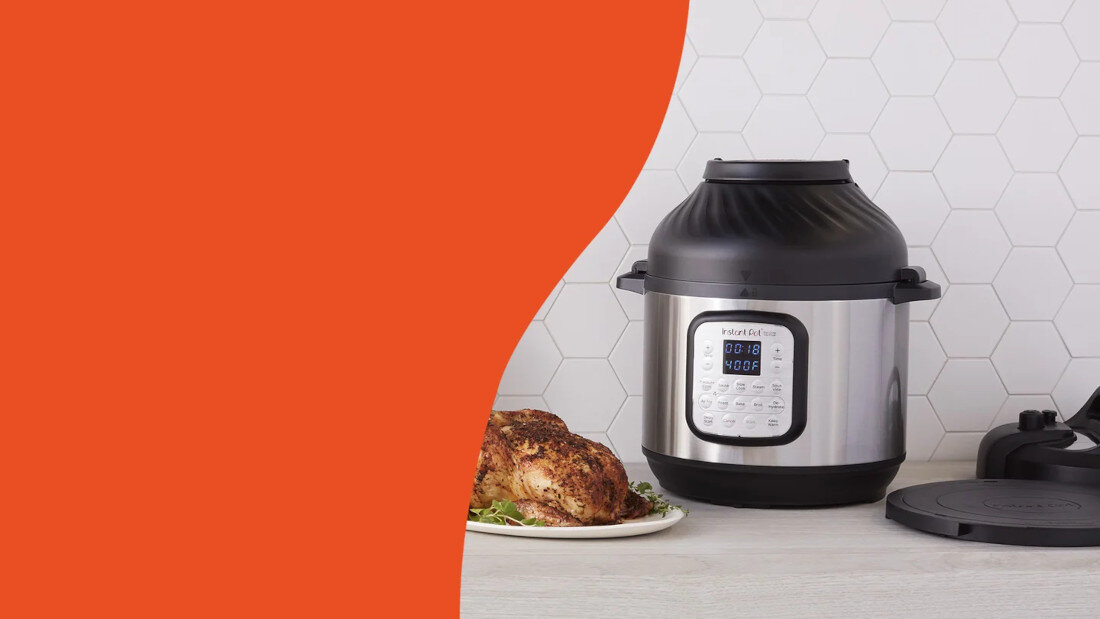 Na blacie kuchennym stoi multicooker z wyświetlaczem cyfrowym, obok którego znajduje się pieczony kurczak na talerzu. W tle widoczna jest biała ściana z sześciokątnymi płytkami.