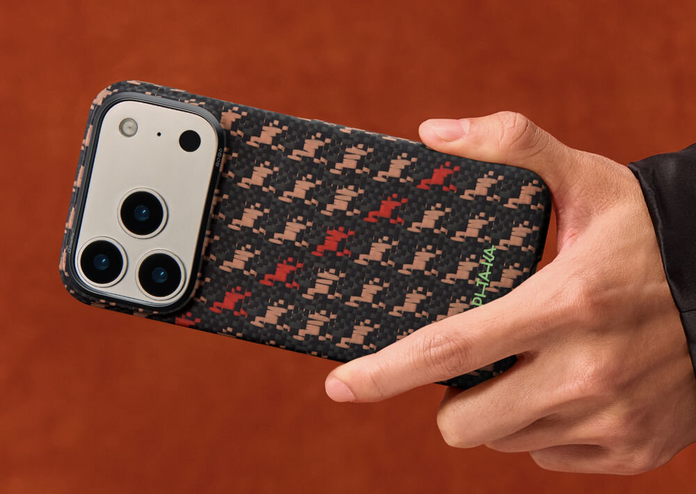 Osoba trzyma telefon w etui o wzorze w kratkę z kolorami czarnym, czerwonym i beżowym. Na etui widoczny jest napis \'PITAKA\'.