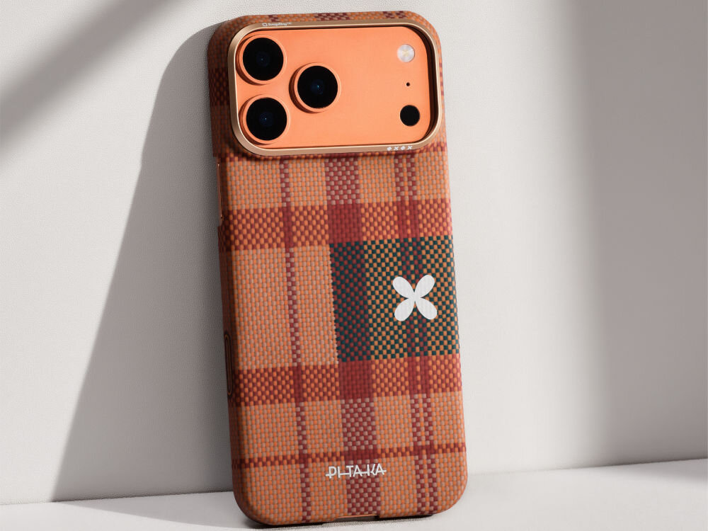 Etui na telefon z wzorem w kratę w odcieniach brązu i pomarańczu, z białym symbolem przypominającym kwiat. Na dole widoczne jest logo \'PITAKA\'.