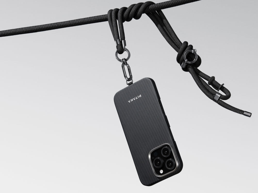 Czarno-szare etui na telefon z logo \'PITAKA\' wisi na czarnym sznurku. Etui ma widoczne wycięcia na aparat z trzema obiektywami.