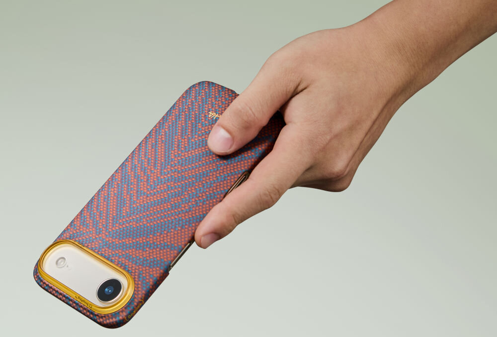 Ręka trzyma telefon w etui o wzorze w jodełkę w kolorach pomarańczowym i niebieskim. Etui ma złotą ramkę wokół aparatu.