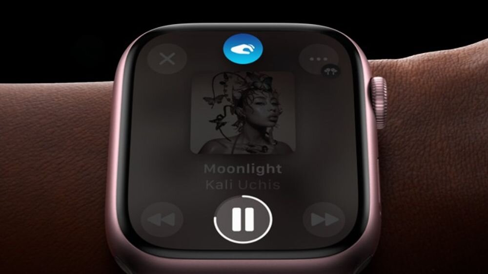 Zbliżenie na ekran zegarka z wyświetloną okładką albumu i tekstem \'Moonlight Kali Uchis\'. Na ekranie widoczne są przyciski sterowania muzyką oraz ikona w kształcie chmury na górze.