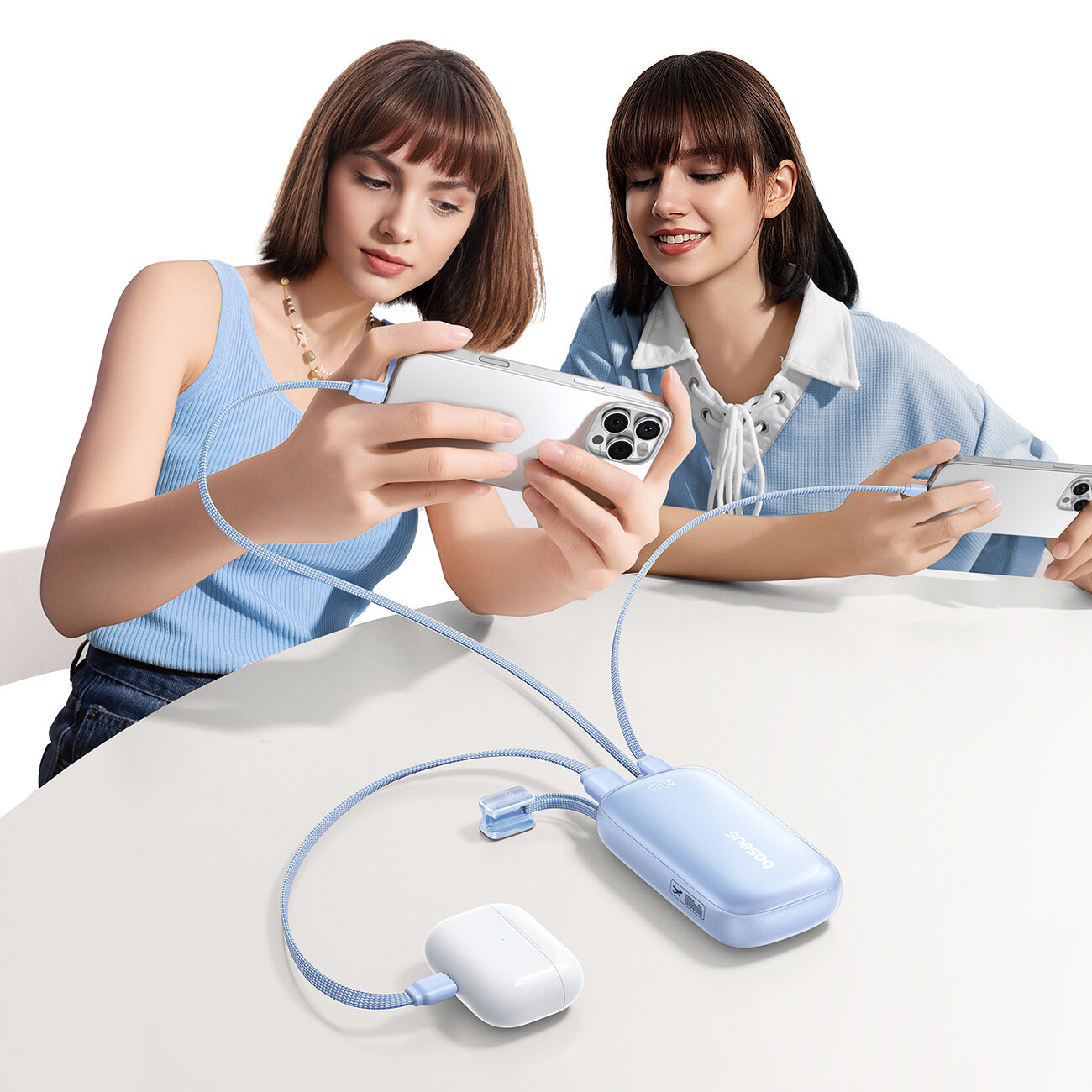 Dwie osoby trzymają smartfony, które są podłączone do niebieskiego powerbanku z logo \'Baseus\'. Powerbank ma dwa kable, jeden z nich jest podłączony do białego etui na słuchawki.