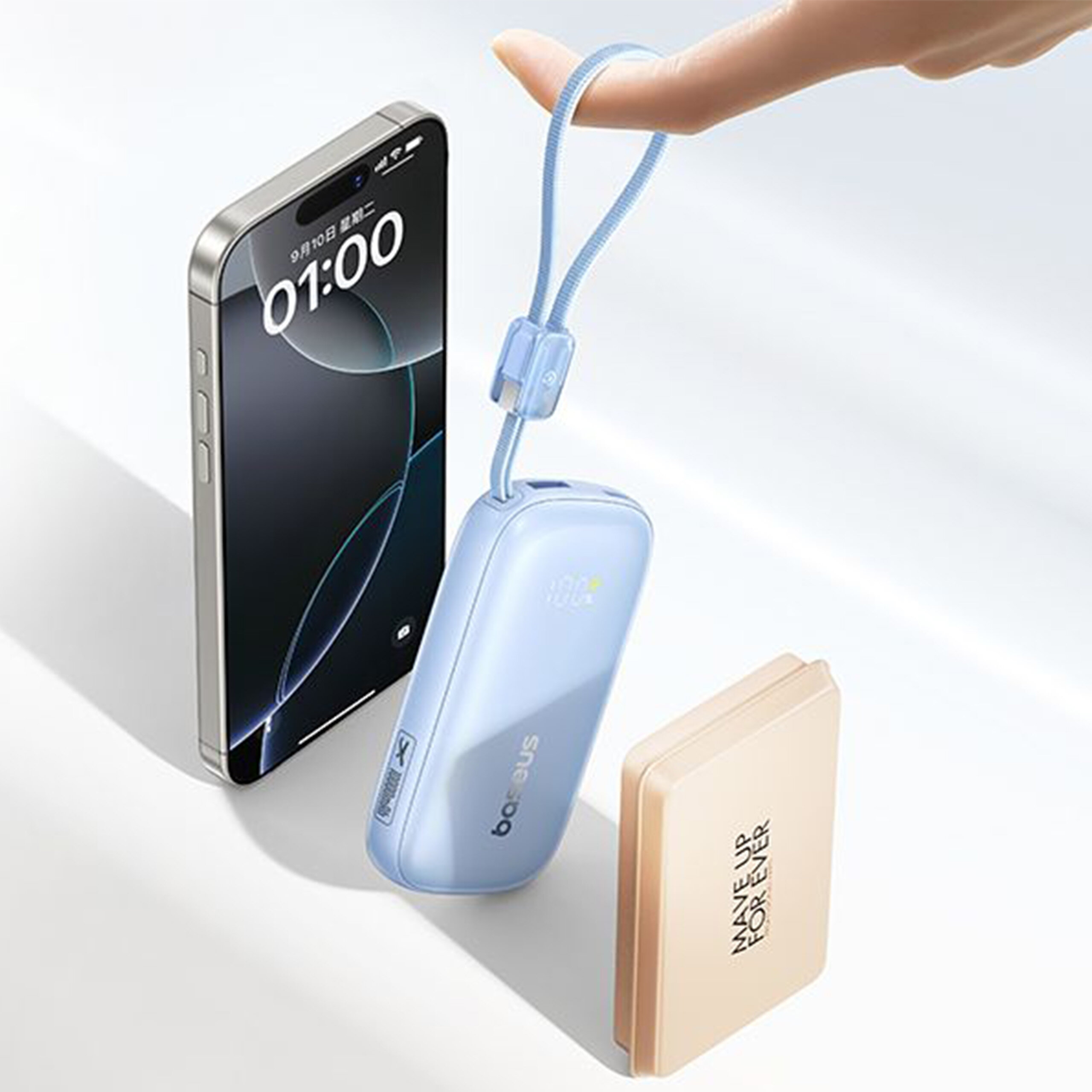 Na obrazie widoczny jest smartfon z wyświetlaczem pokazującym godzinę 01:00 oraz data 9/10. Obok znajduje się niebieski powerbank z napisem \'baseus\' i beżowy przedmiot z napisem \'MAKE UP FOREVER\'.
