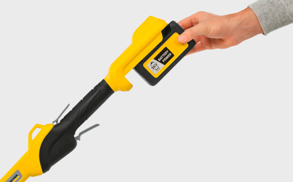 Osoba trzyma akumulator oznaczony jako \'36V Battery Power\' i wkłada go do żółto-czarnego urządzenia ogrodowego.