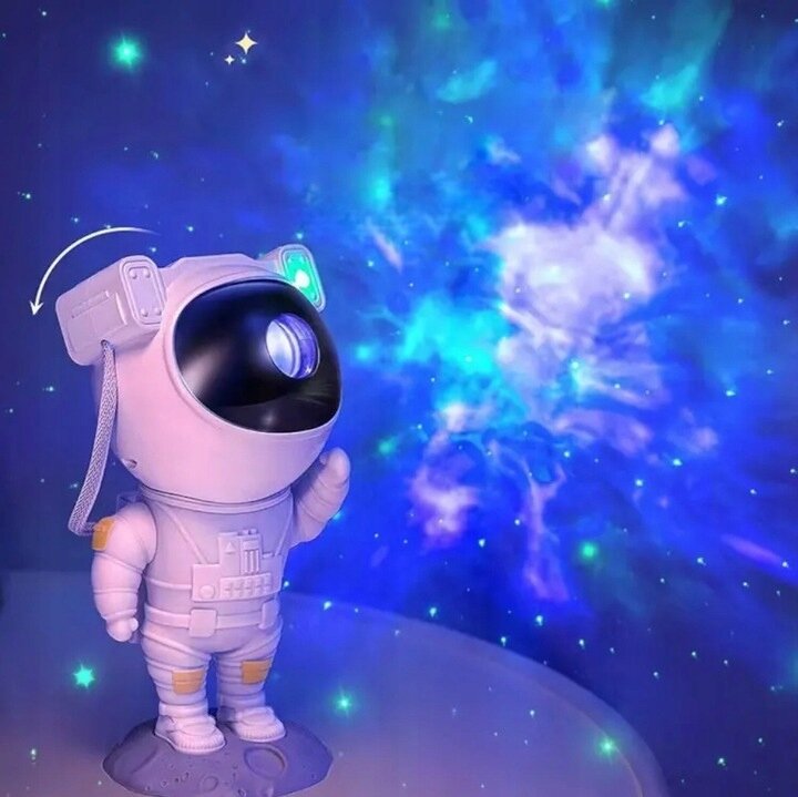 Figurka astronauty z projektorem gwiazd, emitująca niebiesko-zielone światło na ścianę, tworząc efekt kosmicznej mgławicy.