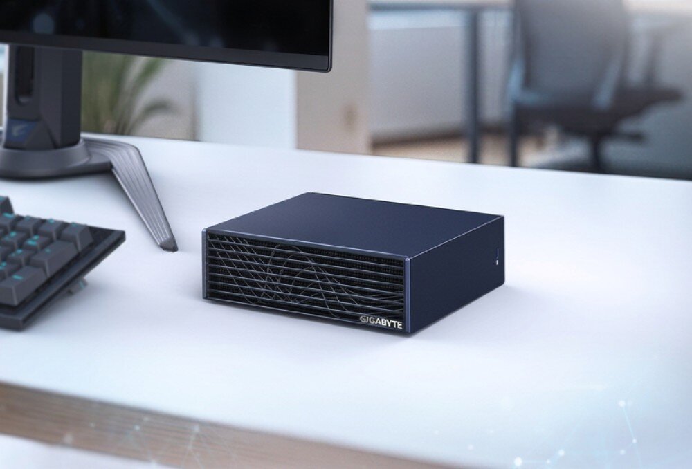 Komputer GIGABYTE AI Top Atom ARM Kompaktowe urządzenie w kształcie prostopadłościanu stojące na biurku obok monitora i klawiatury