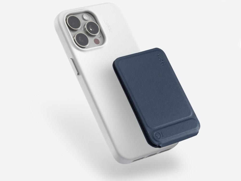 Na obrazie widoczny jest biały telefon z trzema obiektywami aparatu oraz granatowy stojak magnetyczny przymocowany do jego tylnej części. Na stojaku widnieje napis \'MOFT\'.