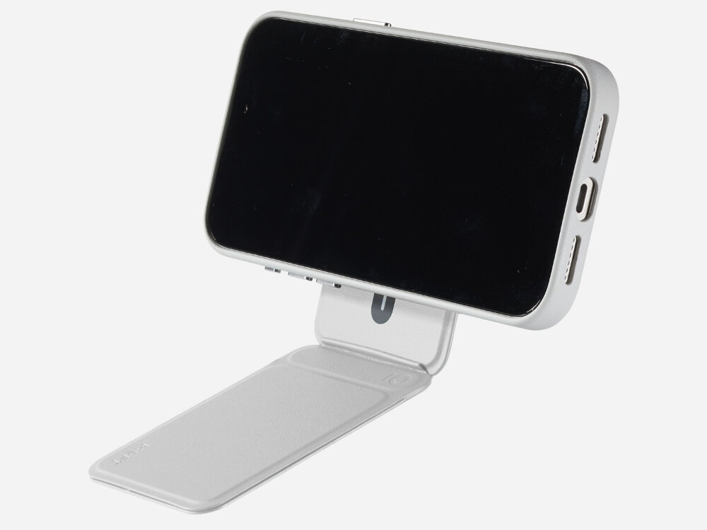 Szary stojak na telefon z funkcją MagSafe, na którym zamocowany jest smartfon. Stojak ma prostokątną podstawę i uchwyt, który podtrzymuje urządzenie w pozycji poziomej.