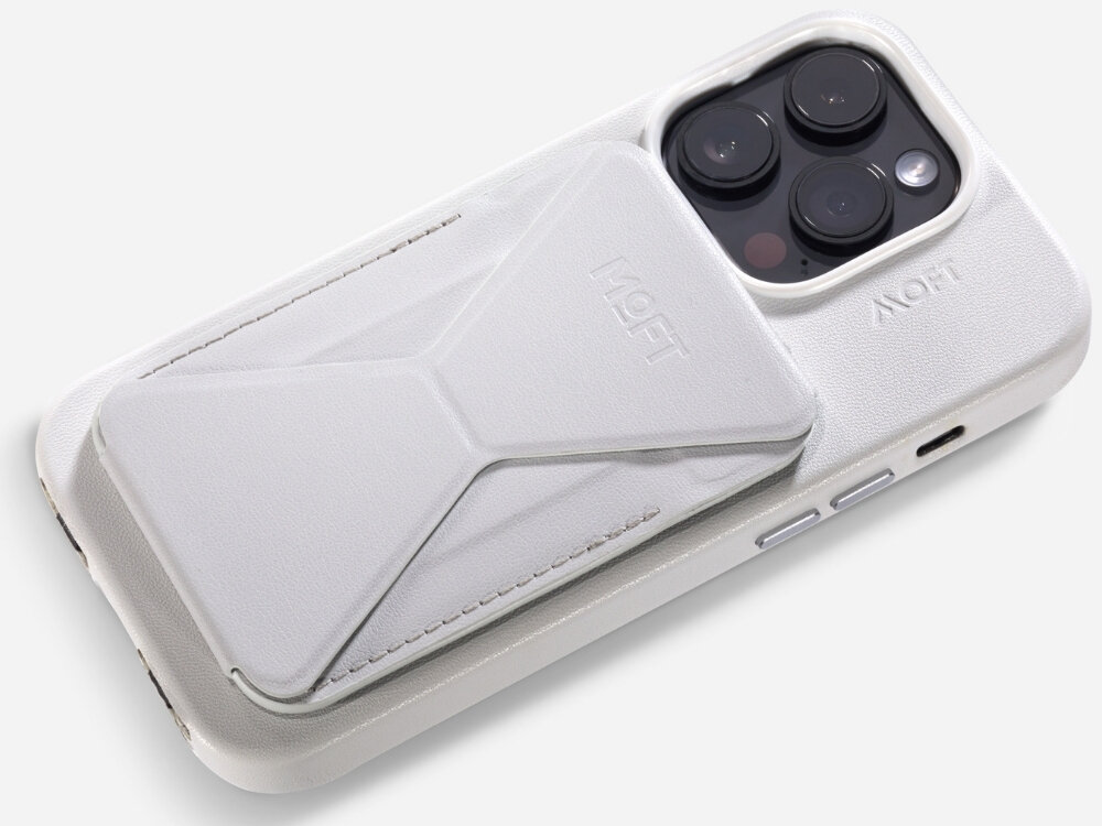 Na zdjęciu widoczny jest szary portfel MOFT Movas Snap-On MagSafe przymocowany do tylnej części telefonu. Na portfelu i etui telefonu znajduje się logo \'MOFT\'.