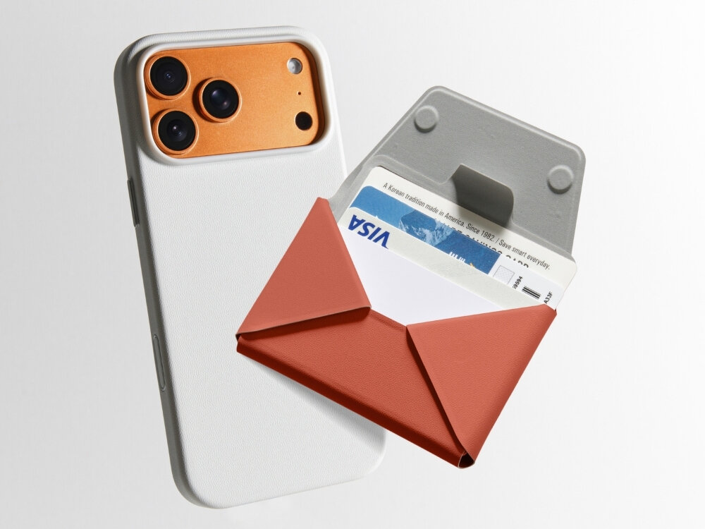 Na obrazie widoczny jest telefon z trzema obiektywami aparatu oraz bordowy portfel MagSafe z kartą płatniczą z napisem \'VISA\'.