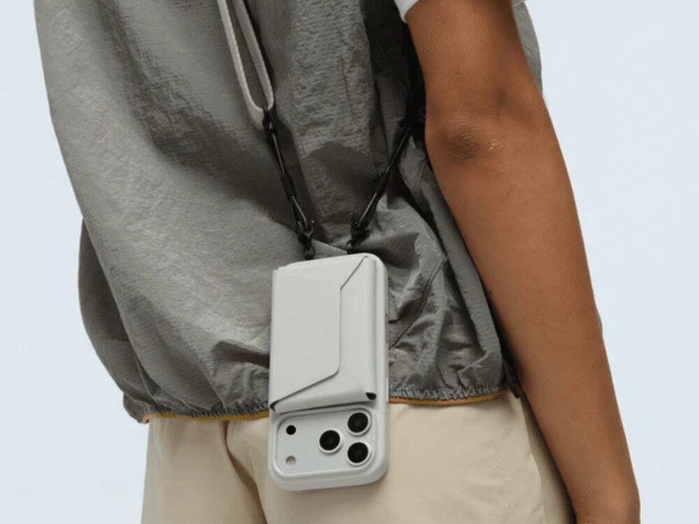 Osoba nosi szary portfel MOFT Agile Travel MagSafe zawieszony na pasku, przymocowany do telefonu z trzema widocznymi obiektywami aparatu.