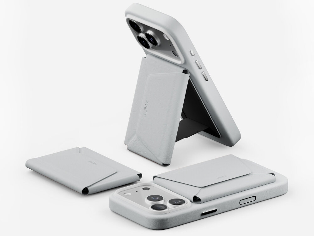 Na obrazie widoczne są trzy szare portfele MagSafe, z których jeden jest przymocowany do telefonu i ustawiony jako stojak. Na portfelach widnieje napis \'MOFT\'.