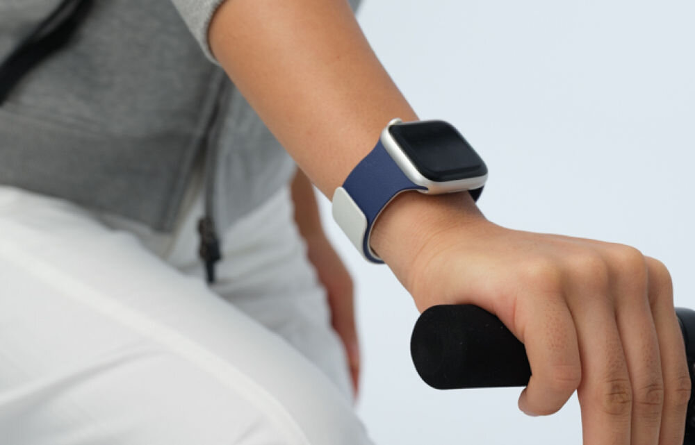 Osoba trzymająca kierownicę roweru ma na nadgarstku granatowy pasek do zegarka Apple Watch.