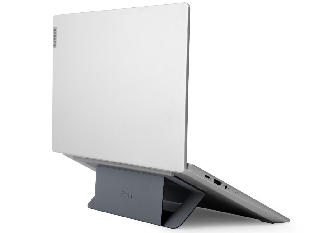 Na zdjęciu widać laptopa ustawionego na szarej podstawce, która unosi jego tył. Na obudowie laptopa widoczne jest logo \'lenovo\', a na podstawce napis \'MOFT\'.