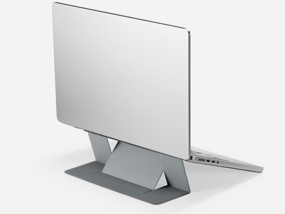 Na obrazie widoczna jest szara podstawka pod laptopa, na której umieszczony jest laptop. Na podstawce znajduje się napis \'MOFT\'.