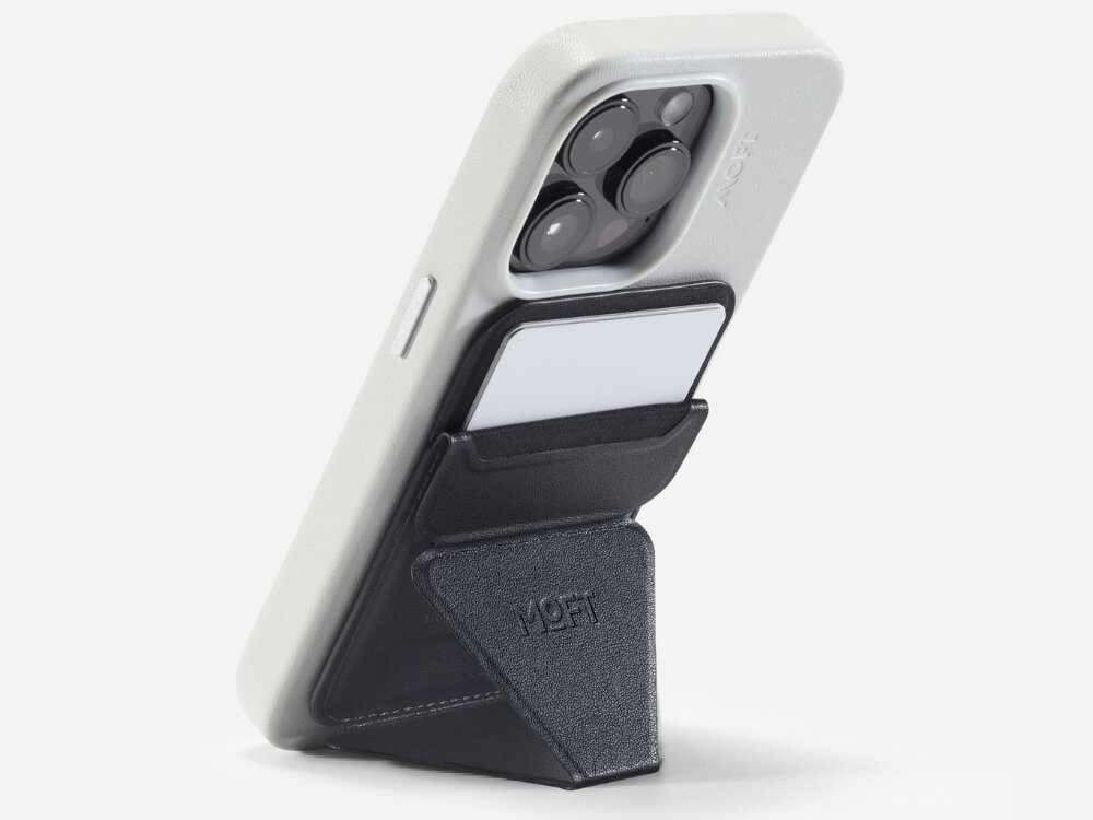 Na zdjęciu widać czarny portfel MOFT Movas Snap-On MagSafe przymocowany do tylnej części telefonu w białym etui. Portfel ma kieszeń na kartę i widoczne logo MOFT.