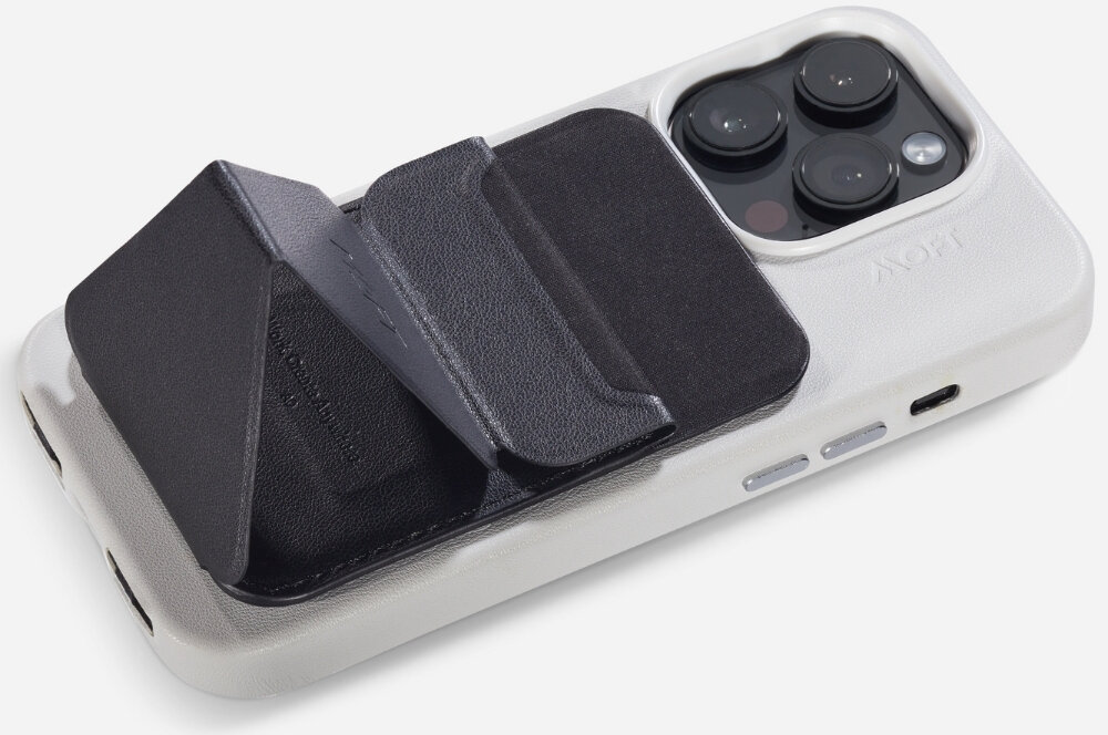 Czarny portfel MagSafe przymocowany do białego etui na telefon z trzema widocznymi obiektywami aparatu. Na portfelu widoczny jest napis \'MOFT\'.