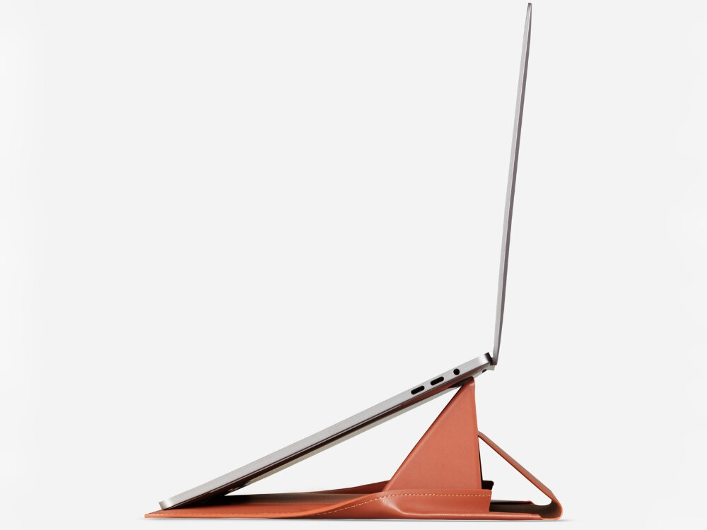 Na obrazie widoczny jest laptop ustawiony na brązowej podstawce, która unosi go pod kątem. Podstawka ma trójkątny kształt i jest wykonana z materiału przypominającego skórę.