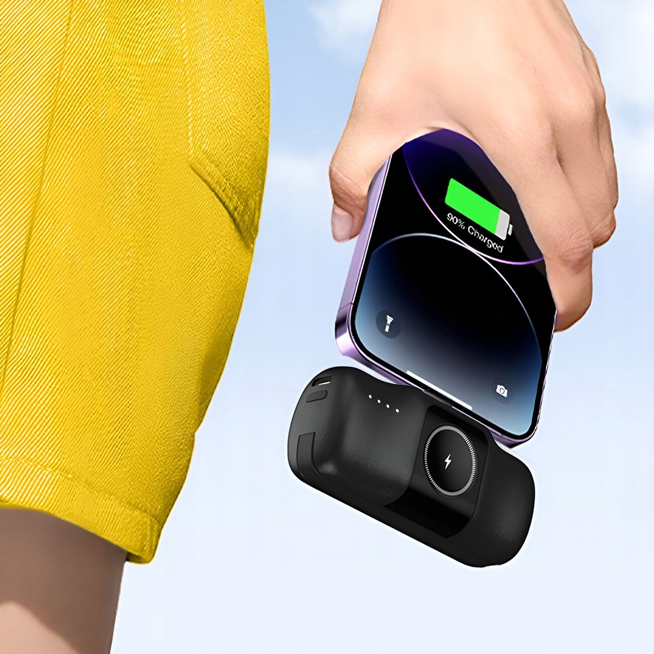 Osoba trzyma w ręce czarny powerbank z okrągłym symbolem błyskawicy. Na ekranie urządzenia widoczny jest wskaźnik naładowania z napisem \'90% Charged\'.
