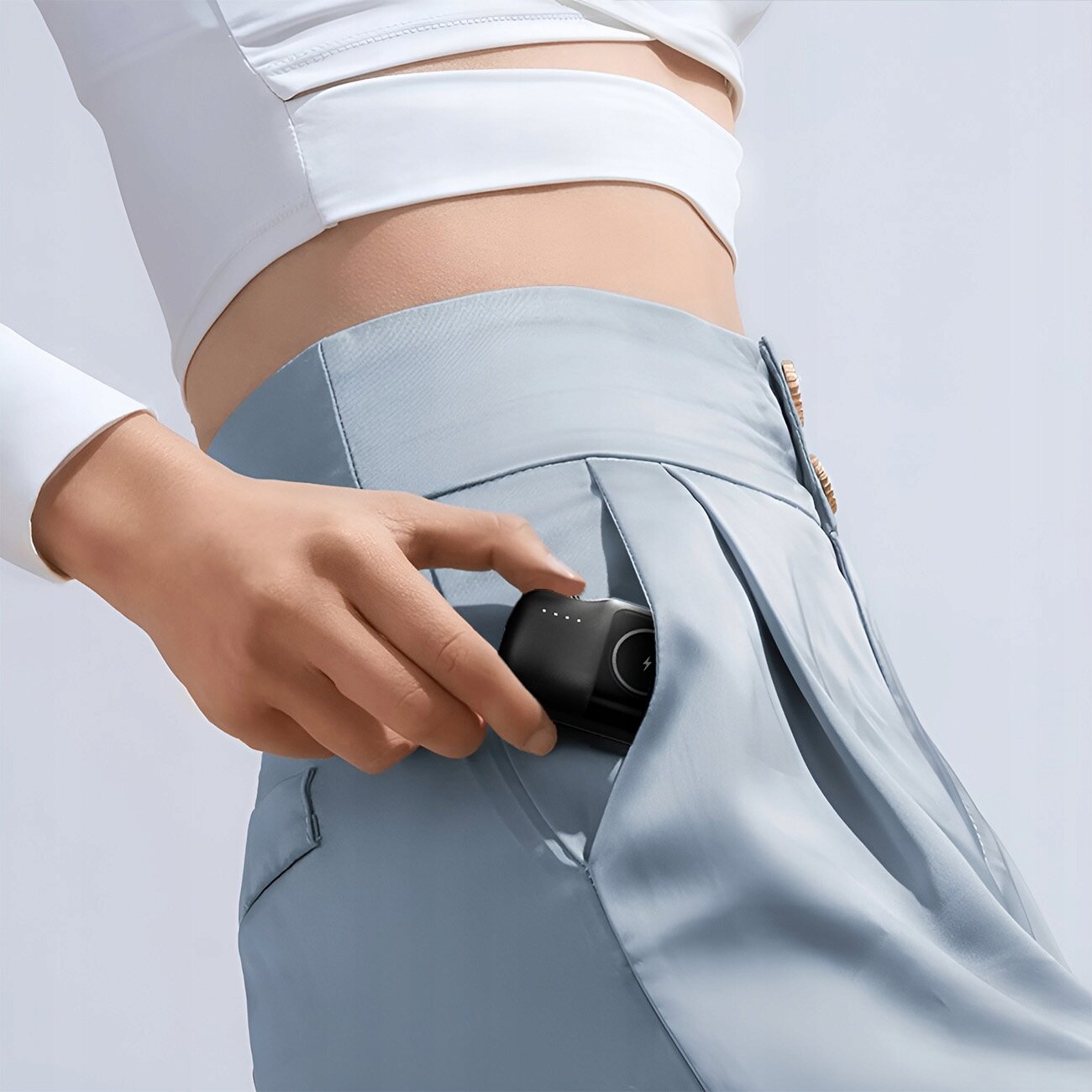 Osoba wkłada czarny powerbank do kieszeni jasnoniebieskich spodni. Powerbank ma okrągły symbol z plusem i cztery małe diody.