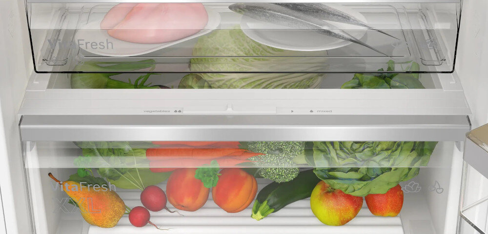 Wnętrze lodówki z widocznymi półkami wypełnionymi różnymi produktami spożywczymi, takimi jak warzywa, owoce, mięso i ryby. Na szufladach widoczny napis \'Fresh\'.