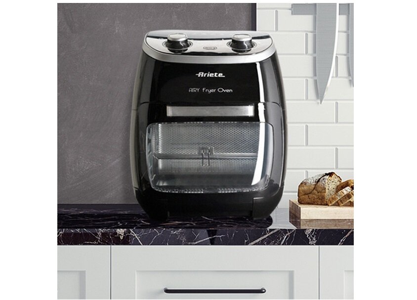 Czarna frytkownica beztłuszczowa z napisem \'Ariete Airy Fryer Oven\' stoi na blacie kuchennym. W tle widoczne są białe płytki i nóż kuchenny.