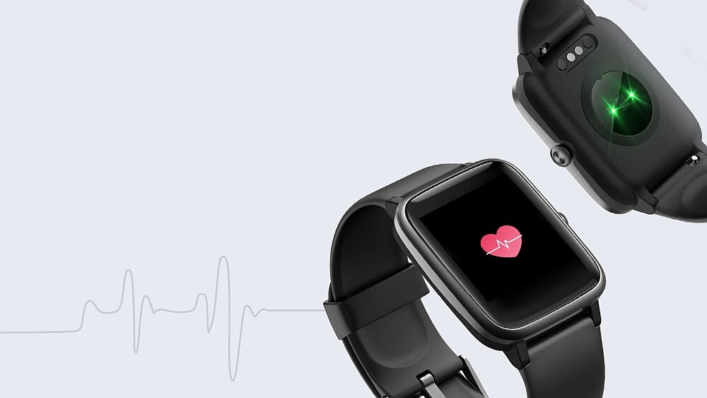 Na obrazie widoczny jest smartwatch z czarnym paskiem, na którego ekranie wyświetla się ikona serca. W tle widać wykres EKG oraz tylną część zegarka z zielonym światłem czujnika.